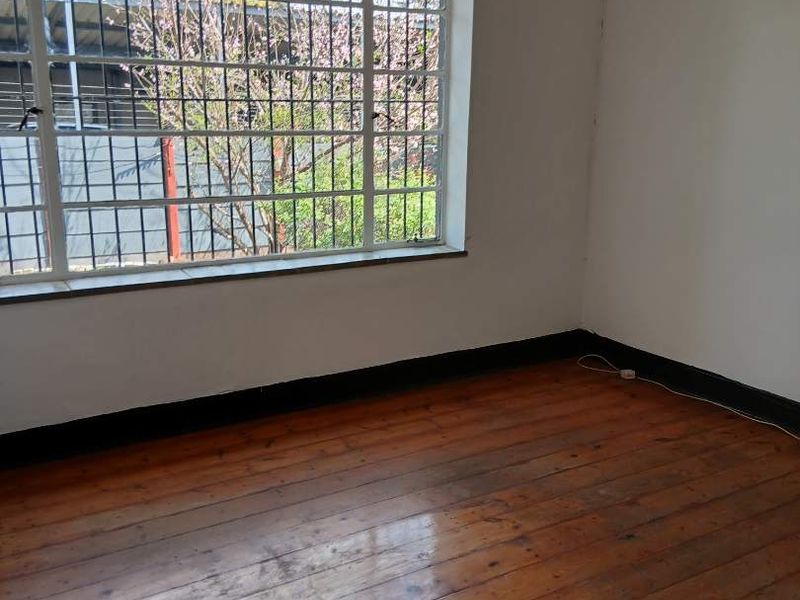 An empty bedroom featuring original timber flooring, large window with security bars, and white walls requiring minor cosmetic attention.