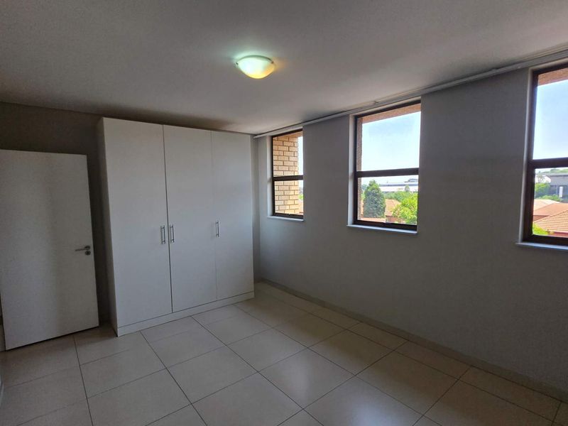 A bright and spacious bedroom featuring neutral tiled flooring, a built-in wardrobe, and large windows providing ample natural light.
