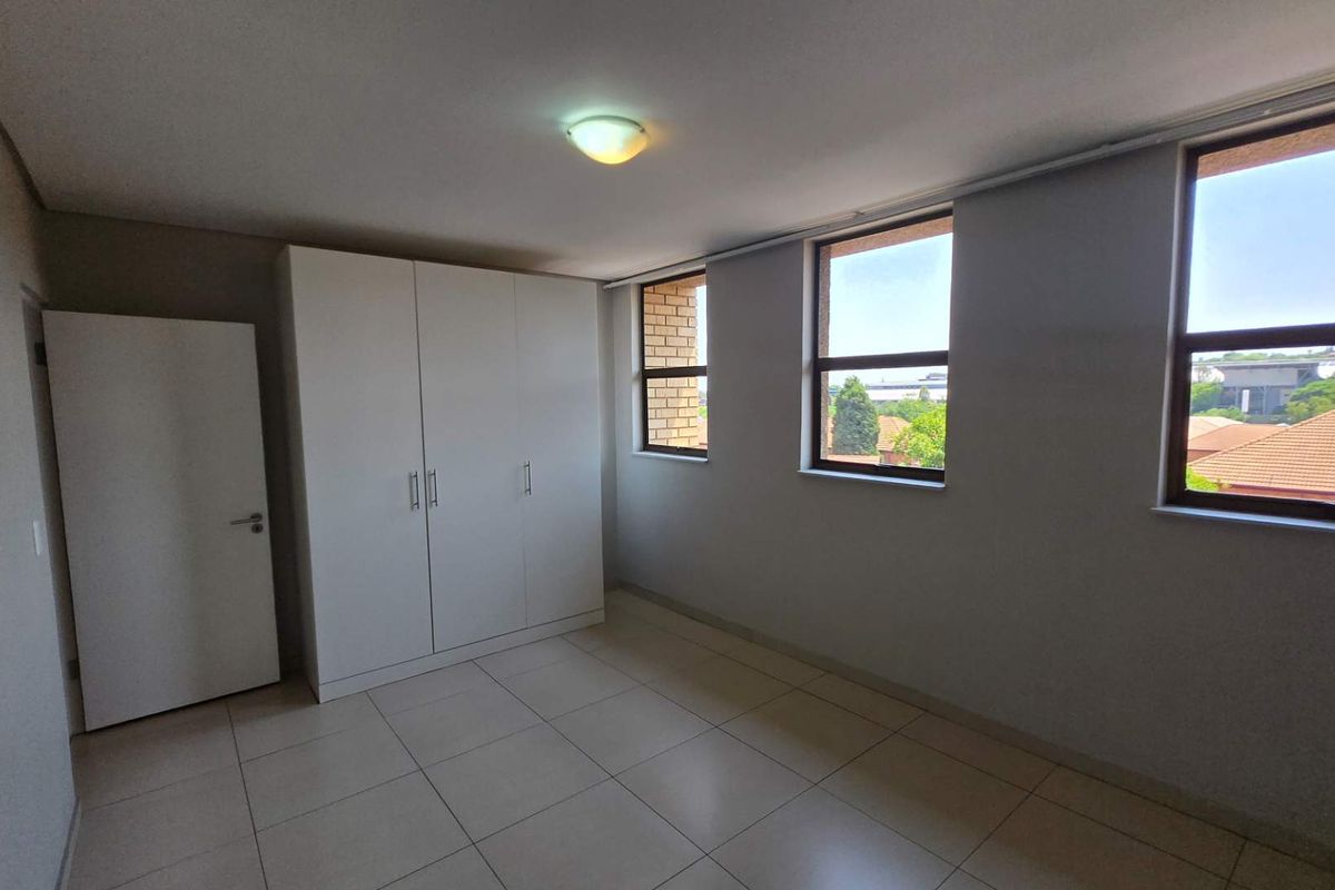 A bright and spacious bedroom featuring neutral tiled flooring, a built-in wardrobe, and large windows providing ample natural light.