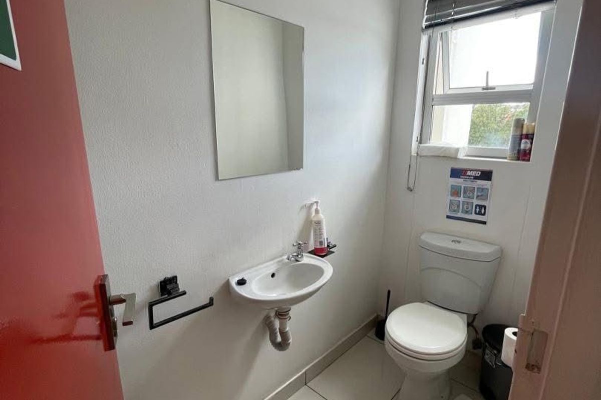 A compact office restroom featuring a wall-mounted basin, a standard toilet, and tiled flooring.