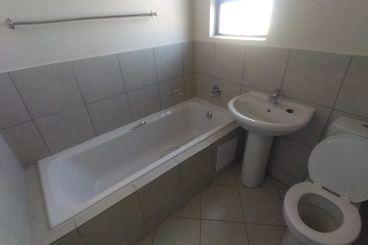 A functional bathroom featuring a built-in bathtub, pedestal basin, and toilet with neutral wall and floor tiling.