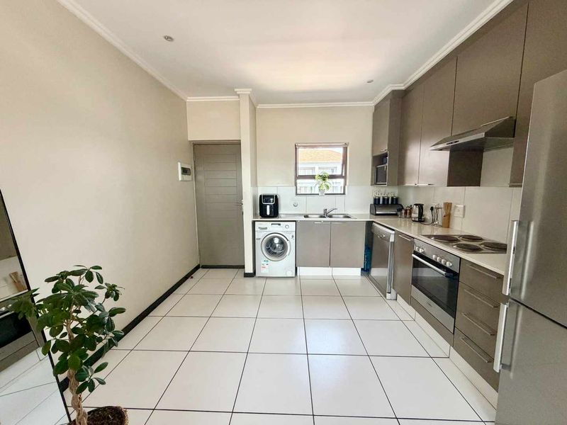 Modern kitchen featuring sleek cabinetry, integrated appliances, tiled flooring, and dedicated plumbing for a washing machine.