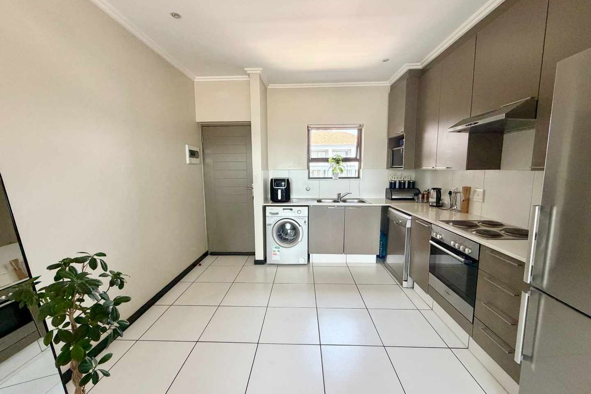 Modern kitchen featuring sleek cabinetry, integrated appliances, tiled flooring, and dedicated plumbing for a washing machine.