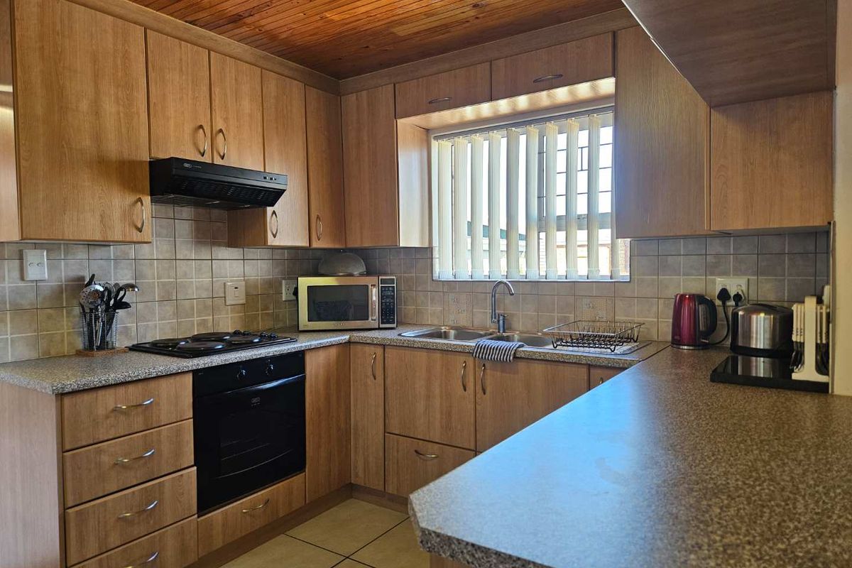 A functional kitchen featuring wood-look cabinetry, laminate countertops, a built-in oven, gas hob, extractor fan, and a double sink with tiled splashbacks.