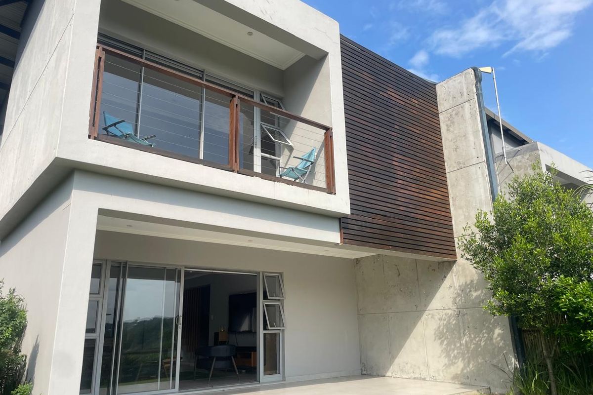 Modern two-story residence featuring a ground floor patio with sliding glass doors and an upper-level balcony with timber and glass balustrades.