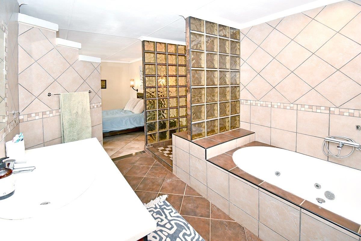 Open-plan bathroom featuring a built-in bathtub, vanity basin, and decorative glass block partition wall with dated ceramic tiling.