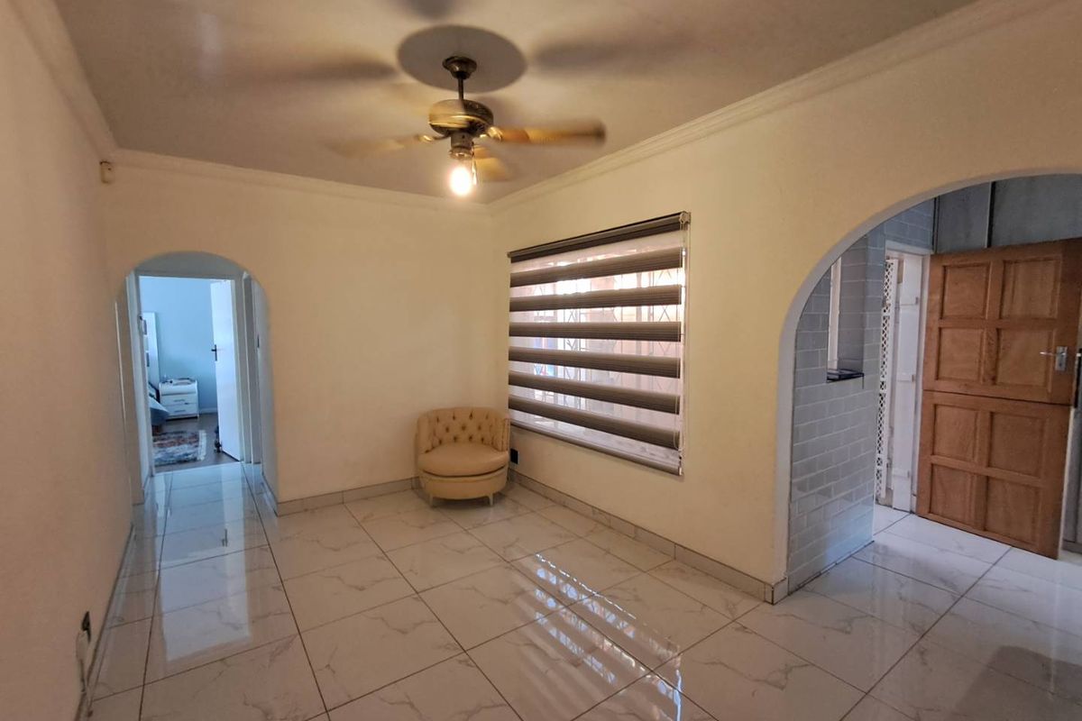 A bright living area featuring polished marble-look floor tiles, arched doorways, a ceiling fan, and modern zebra-style window blinds.