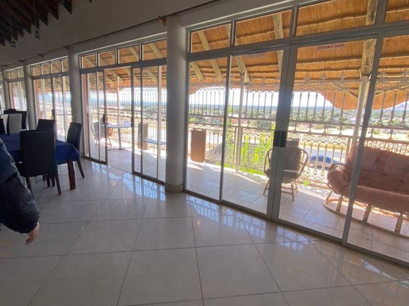 Spacious open-plan area featuring large sliding glass doors, tiled flooring, and an exposed timber beam ceiling with access to a balcony.