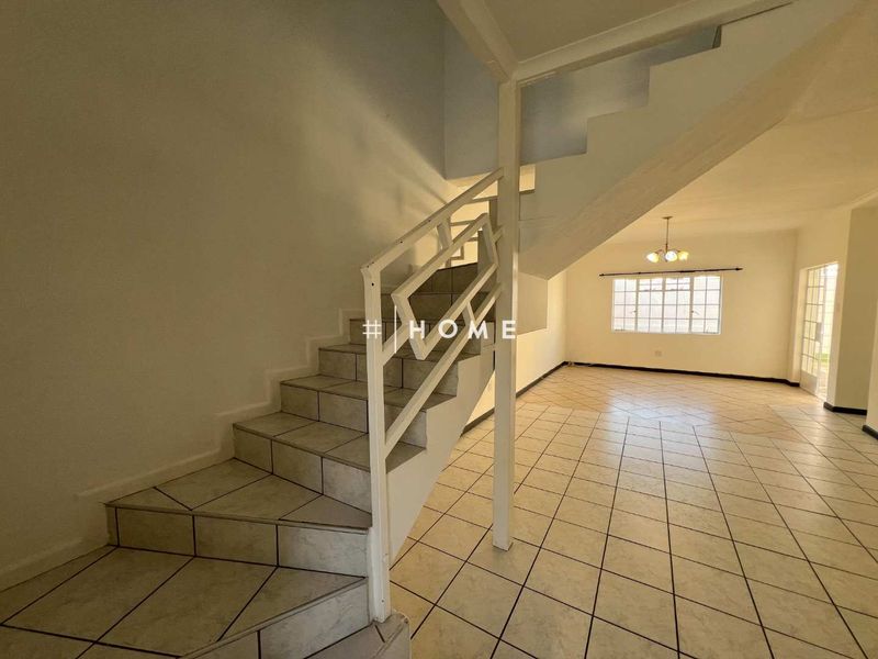 An open-plan living area featuring ceramic floor tiles and a central staircase with a metal balustrade, offering a blank canvas for interior design.