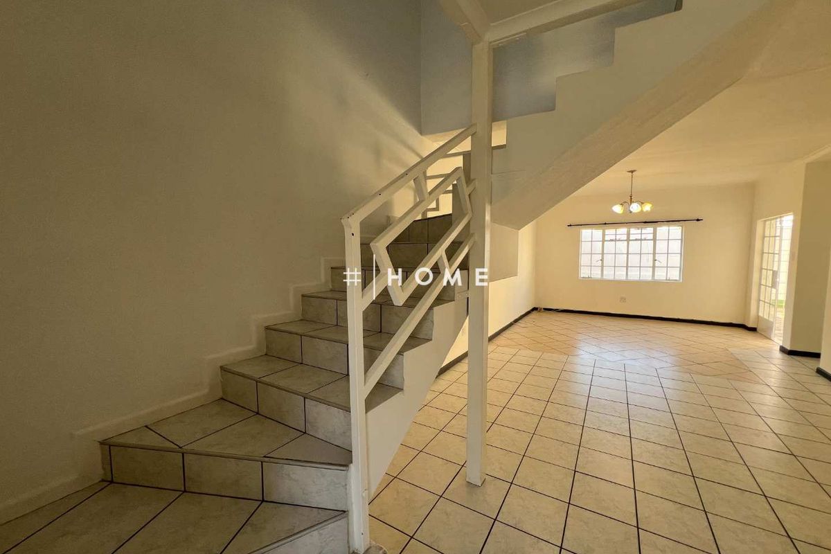 An open-plan living area featuring ceramic floor tiles and a central staircase with a metal balustrade, offering a blank canvas for interior design.