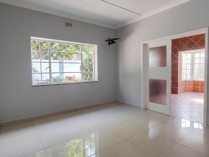 A bright, empty living area featuring polished tiled flooring, neutral walls, and a sliding door leading to an adjacent tiled space.
