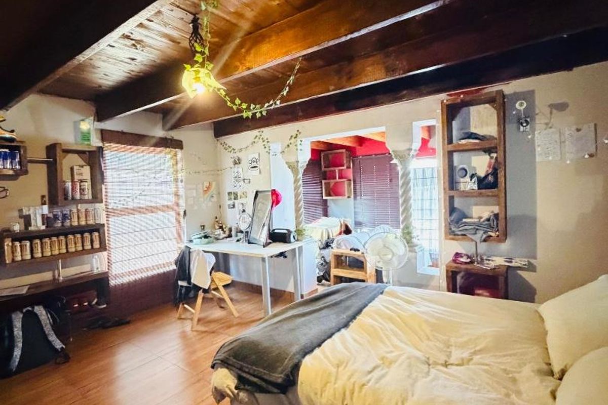 A bedroom featuring exposed timber ceiling beams, wood-look flooring, and built-in shelving units, offering a rustic aesthetic with potential for modern updates.