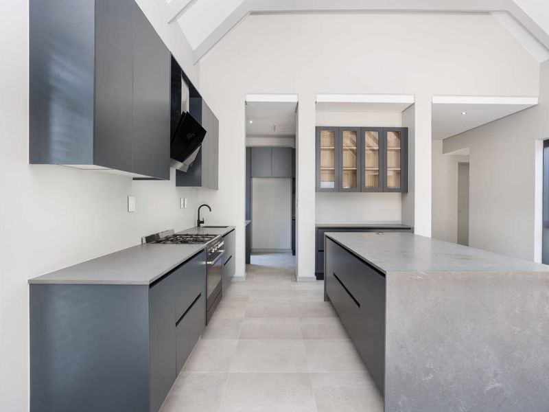 Modern kitchen featuring dark cabinetry, a large central island with stone countertops, high-end built-in appliances, and a spacious vaulted ceiling design.