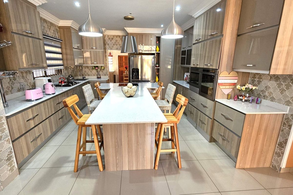 Modern kitchen featuring wood-grain cabinetry, stone countertops, a central island with breakfast bar seating, and integrated double ovens.