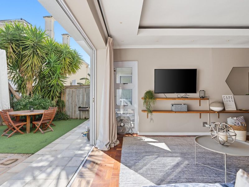 Open plan living area featuring timber flooring and recessed ceiling, seamlessly flowing through large sliding doors to a private paved patio and garden space.