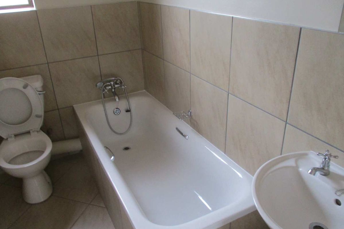 A functional bathroom featuring a bathtub with shower mixer, pedestal basin, and neutral wall and floor tiling.