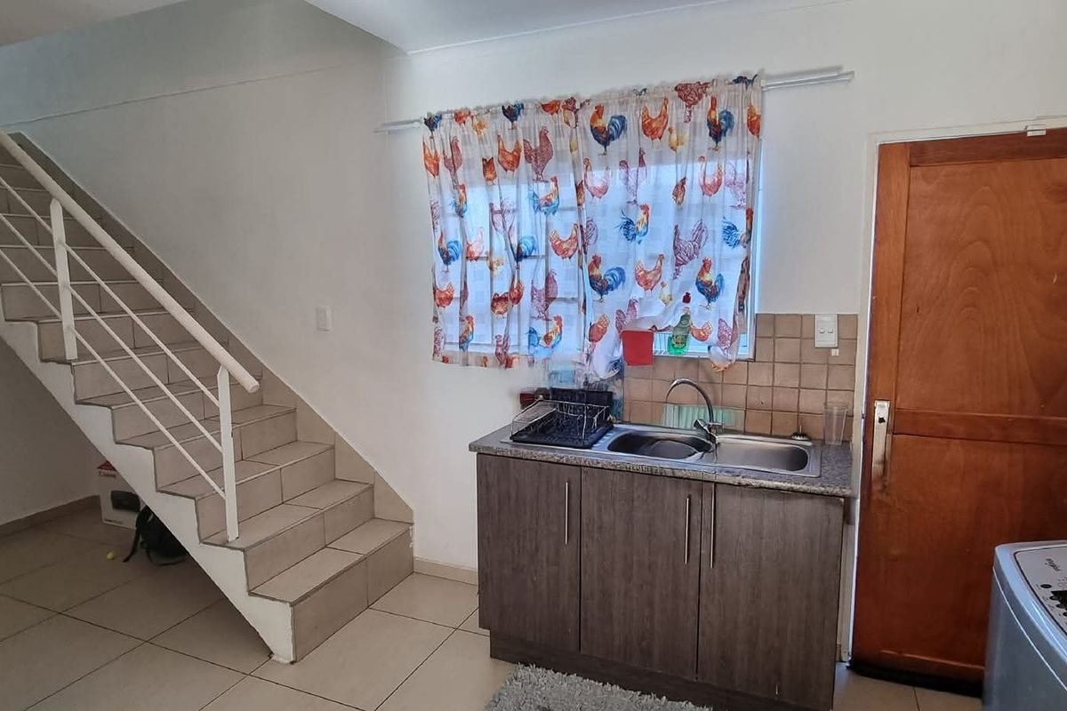 Kitchen area featuring built-in cabinetry, stainless steel sink, and tiled flooring, with an adjacent staircase leading to the upper level.