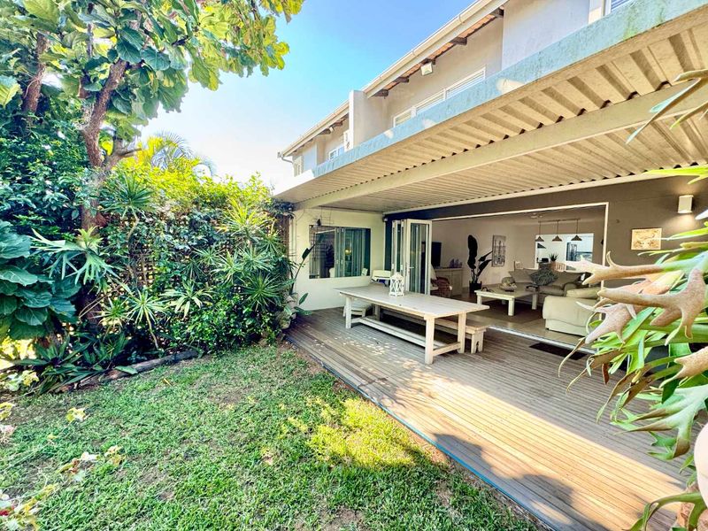 A spacious covered patio featuring timber decking, seamlessly connecting the indoor living area to a private, well-maintained garden through large bi-fold doors.