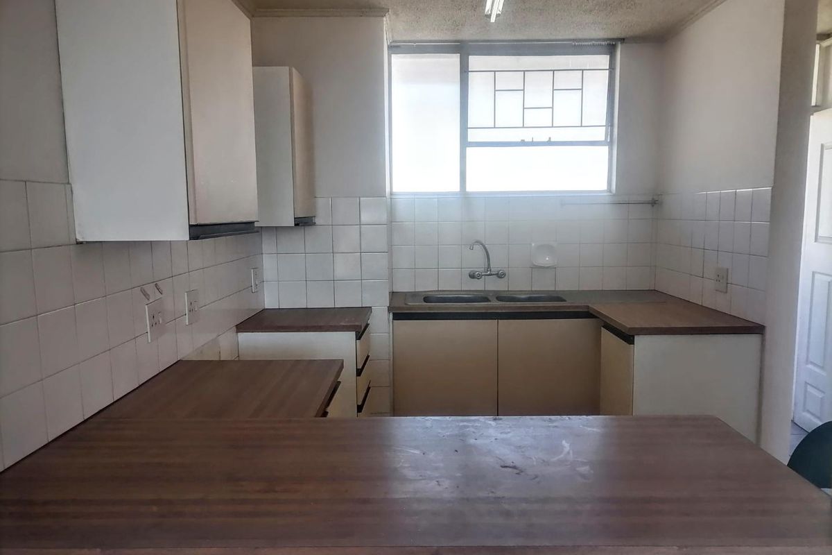 A dated kitchen featuring laminate countertops, a double basin sink, and tiled backsplash, offering a functional layout ready for modernization.