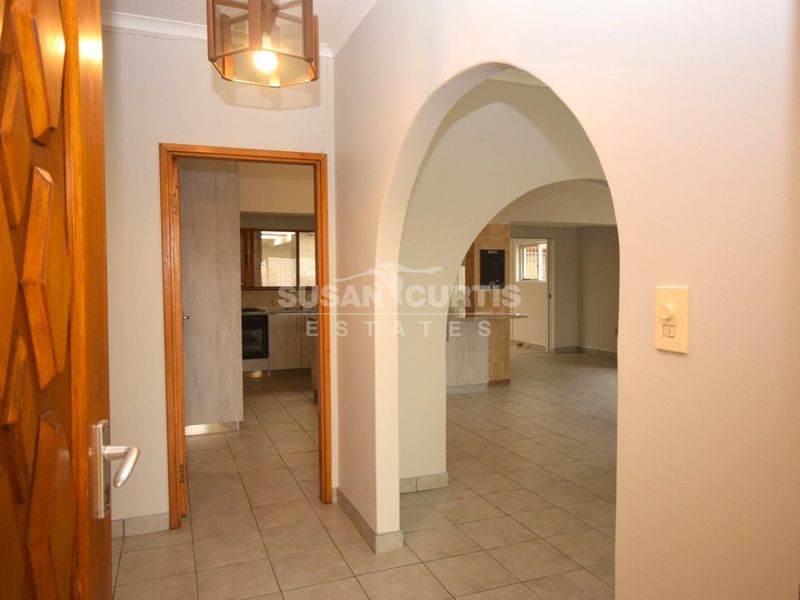 A bright entrance hallway featuring tiled flooring and an arched opening leading into the main living and kitchen areas.