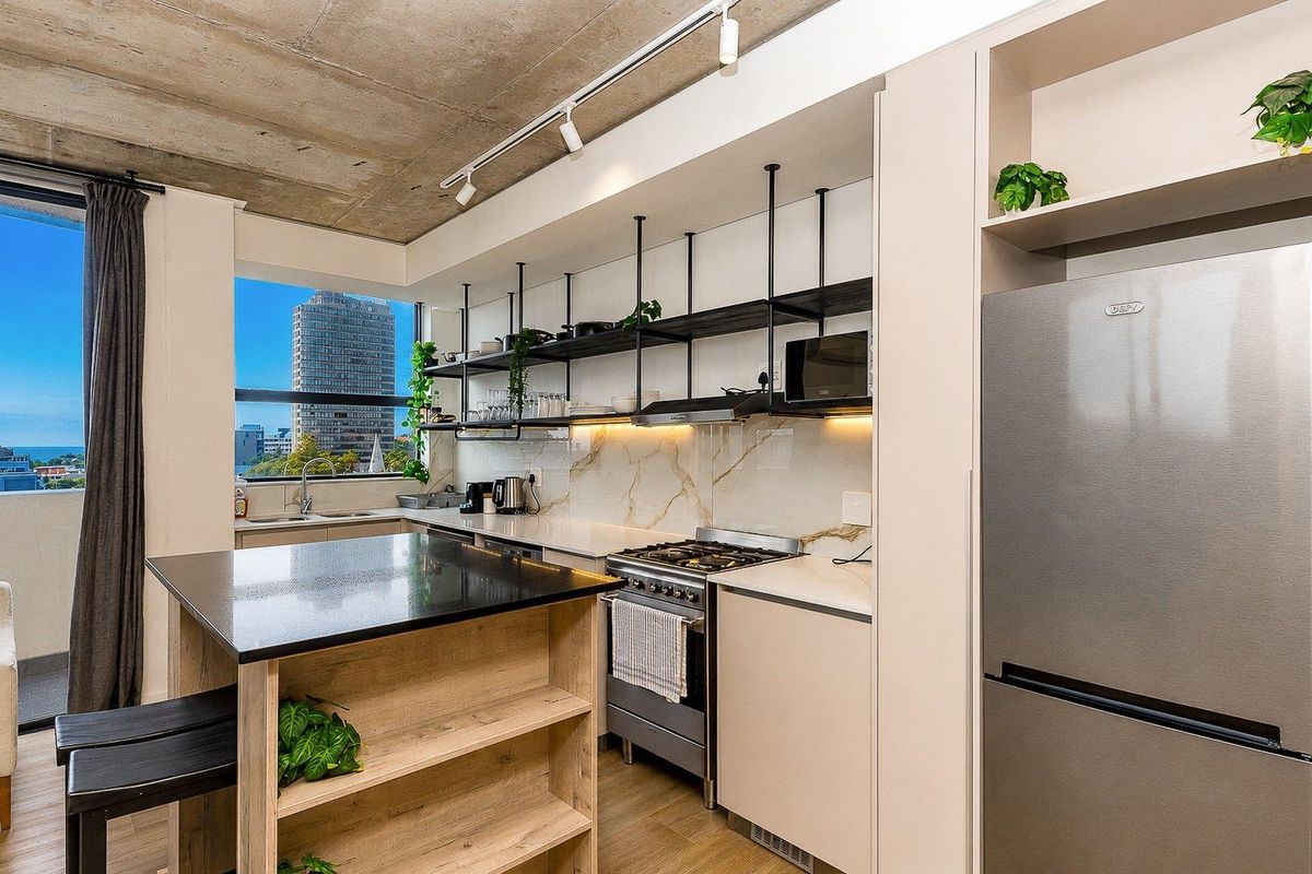 Modern kitchen featuring exposed concrete ceilings, marble-look splashback, gas stove, open shelving, and high-quality stone countertops with integrated cabinetry.