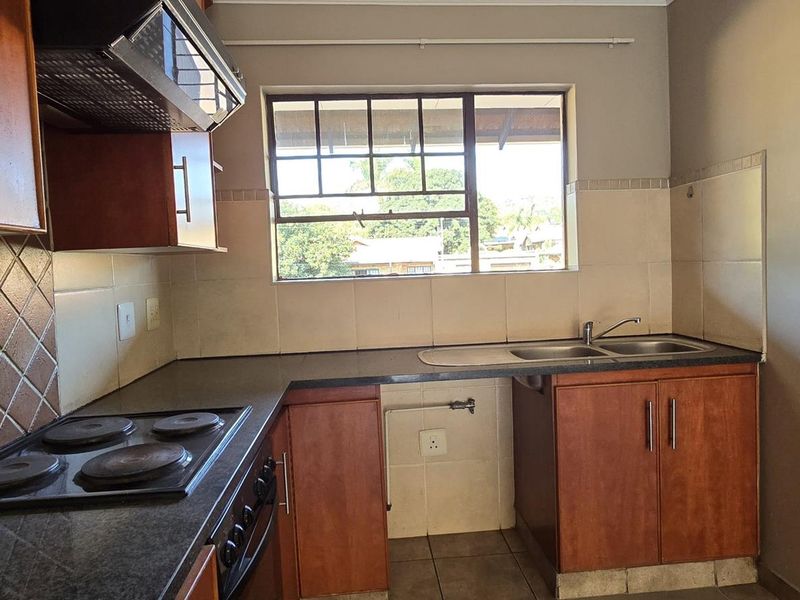 A functional kitchen featuring built-in wooden cabinetry, a dark laminate countertop, an electric hob with extractor fan, and a double sink with tiled backsplash.