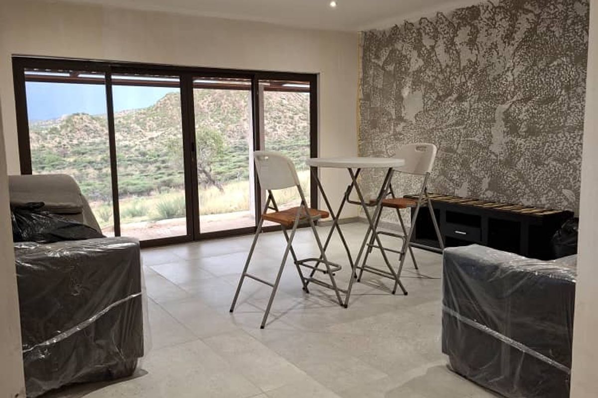 A living area featuring tiled floors, recessed lighting, and large sliding glass doors with scenic views, complemented by a textured feature wall.