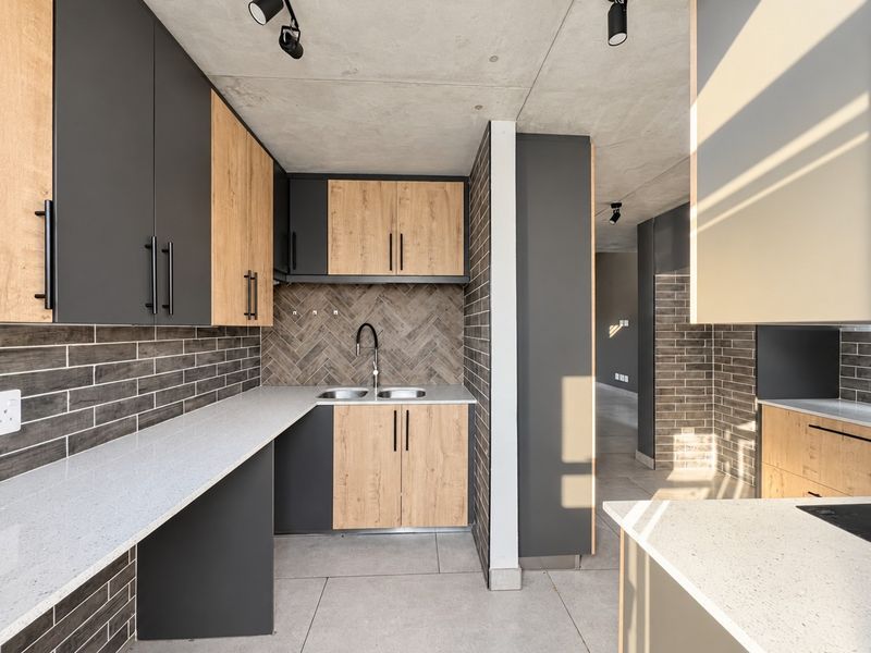 Modern kitchen featuring two-tone cabinetry, stone countertops, herringbone tile backsplash, and exposed concrete ceilings in an open-plan layout.