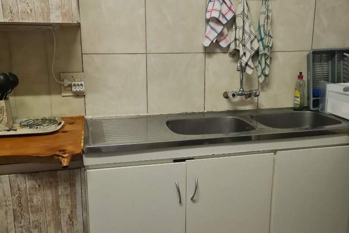 A functional kitchen area featuring a double stainless steel sink, tiled splashback, and built-in cabinetry with wood-effect laminate detailing.