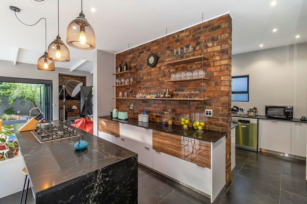 Modern kitchen featuring a central island with gas hob, sleek cabinetry, and a striking exposed brick feature wall with integrated shelving.