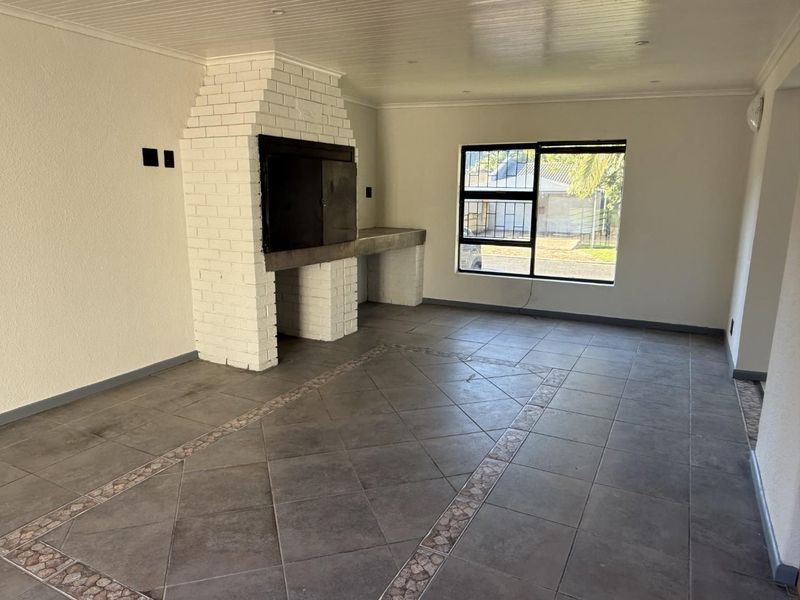 Spacious living area featuring a prominent built-in brick fireplace, tiled flooring with decorative inlay, and large windows with security bars.
