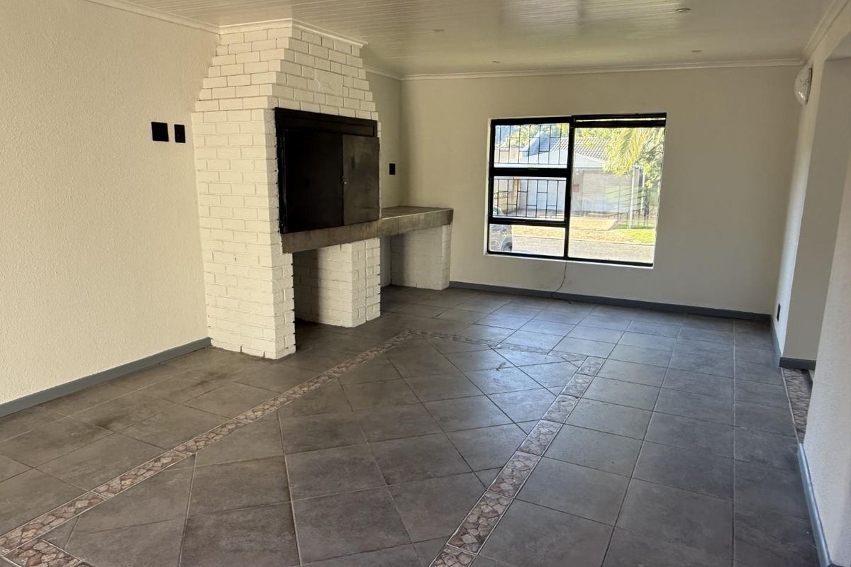 Spacious living area featuring a prominent built-in brick fireplace, tiled flooring with decorative inlay, and large windows with security bars.