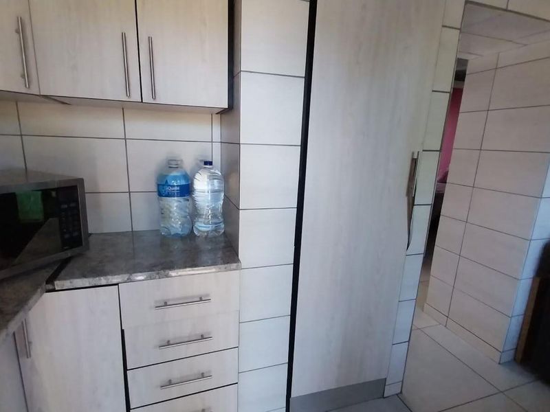 A functional kitchen featuring light-toned cabinetry, tiled backsplash, and tiled flooring, providing a clean and practical workspace.
