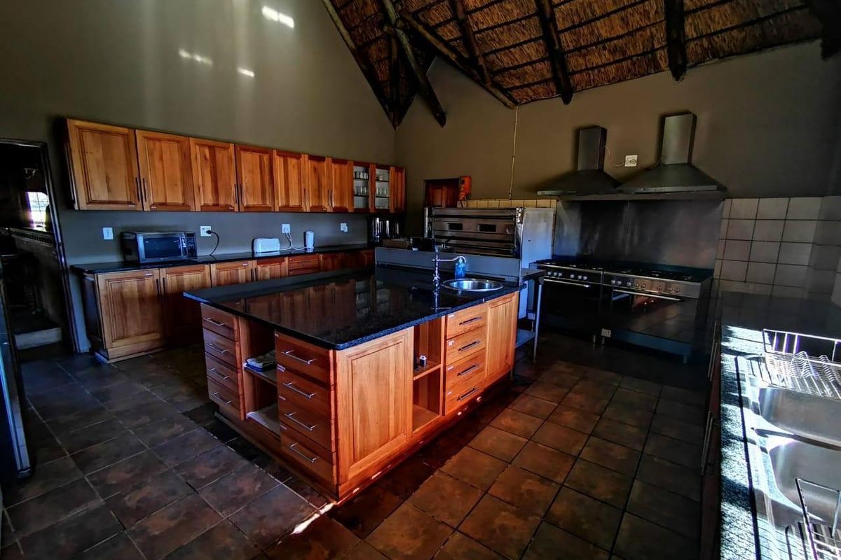 Spacious farmhouse kitchen featuring wooden cabinetry, a large central island with granite countertops, commercial-grade cooking appliances, and a high-volume exposed thatch ceiling.
