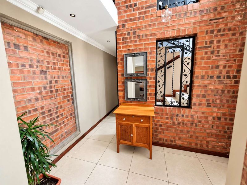 An inviting entrance hall featuring exposed brick walls, tiled flooring, and a decorative wrought iron staircase railing, creating a warm and textured aesthetic.