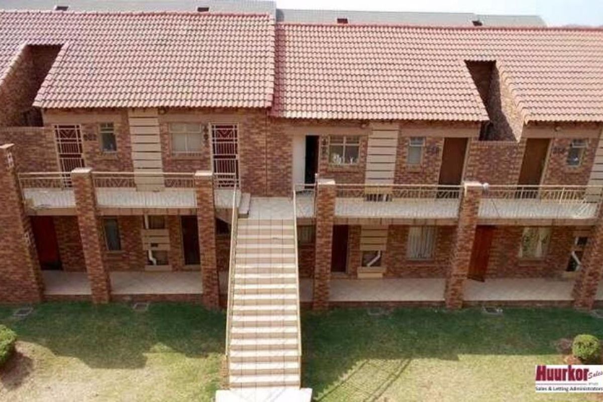 An elevated view of a multi-story apartment complex featuring brick facades, tiled roofing, and shared balcony access with an external staircase.