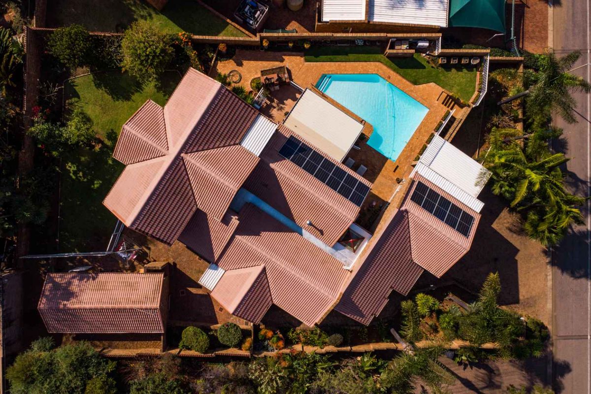 Aerial view of the property showcasing the tiled roof, integrated solar panels, swimming pool, and surrounding garden area.