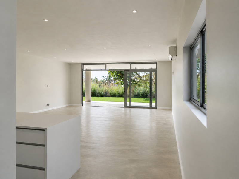 Spacious open-plan living area featuring polished concrete floors, recessed lighting, and large sliding glass doors opening to a private garden.