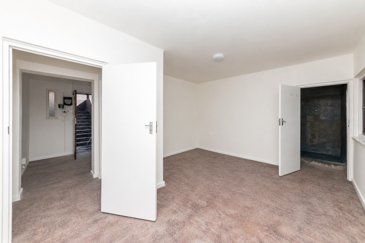 An empty, neutrally painted room featuring vinyl flooring, with an open doorway leading to an adjacent space showing signs of wear.