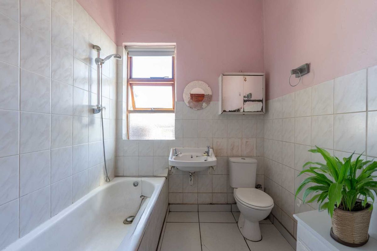 A dated bathroom featuring a standard bathtub with shower attachment, wall-mounted basin, and toilet, requiring cosmetic updates to modernize the space.