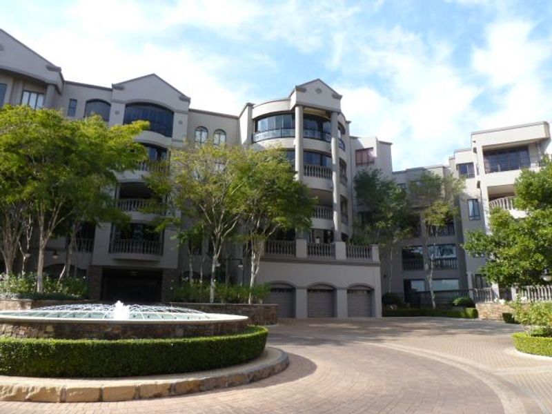 A well-maintained multi-level cluster complex featuring a central stone fountain, paved driveway, and elegant architectural balustrades.
