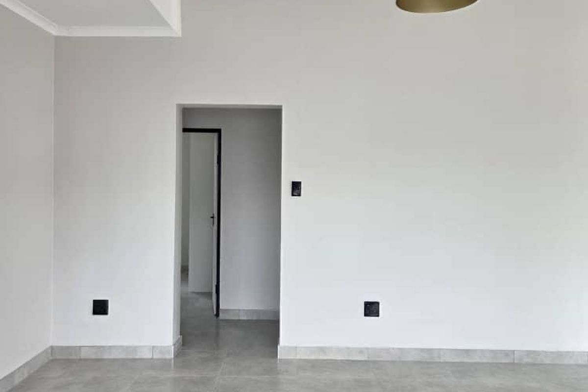 A bright, modern, and empty living space featuring neutral grey floor tiles, clean white walls, and a contemporary pendant light fixture.