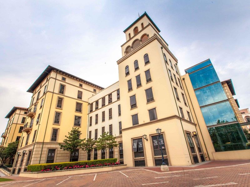 A professional exterior view of a multi-story office building featuring a prominent tower, glass facade, and well-maintained paved driveway and landscaped garden areas.