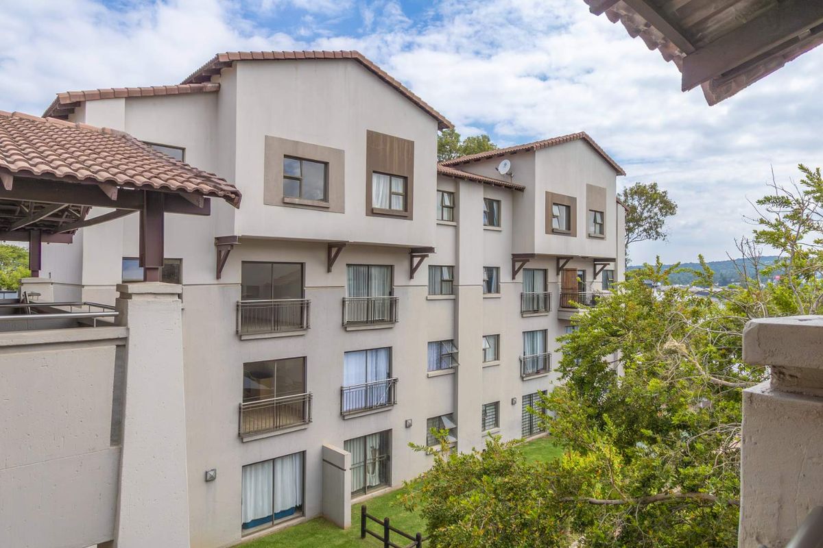 Exterior view of a multi-story apartment complex featuring tiled roofing, balconies with metal railings, and landscaped garden areas.
