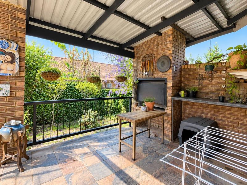 Covered outdoor patio featuring a built-in braai, brick masonry walls, and tiled flooring, overlooking a private garden area.