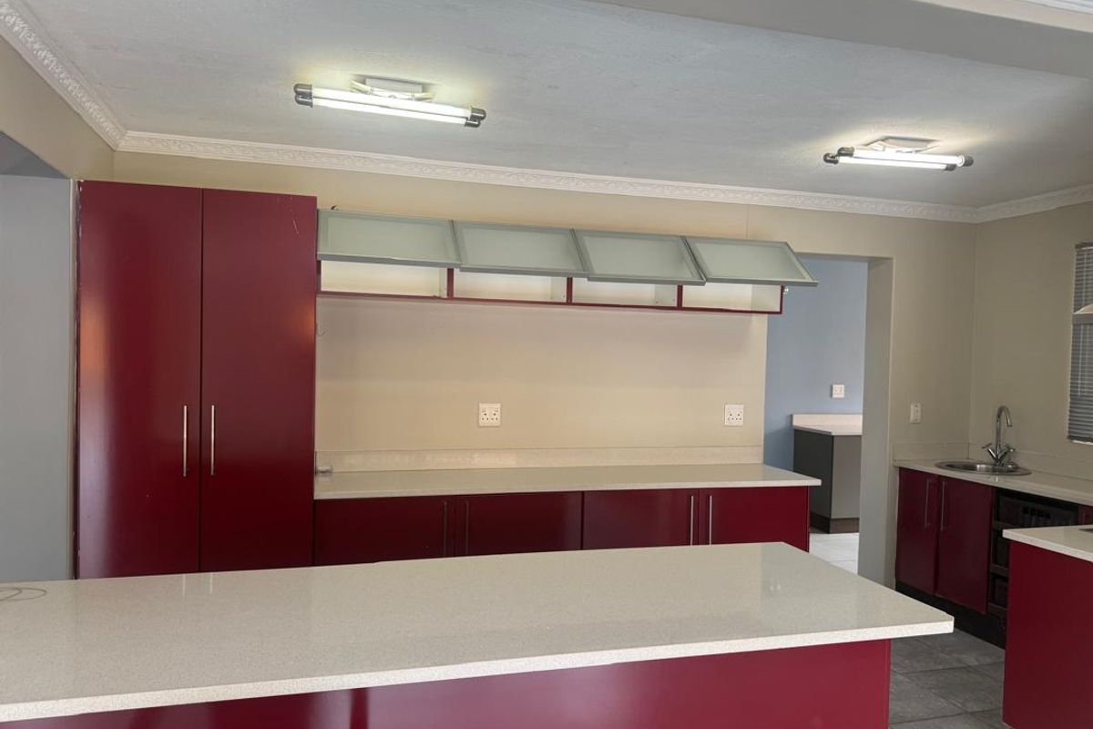 Spacious kitchen featuring red cabinetry, stone countertops, a central island, and ample storage space, offering a functional layout for culinary activities.