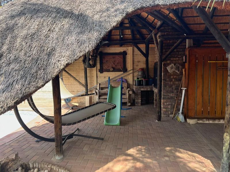 Covered outdoor patio area featuring a traditional thatch roof, exposed timber beams, and a built-in brick braai, perfect for relaxed outdoor entertaining.