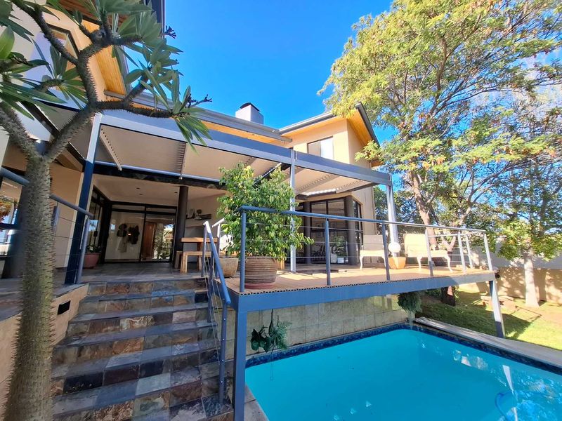 A well-maintained outdoor entertainment area featuring a raised timber deck, covered patio, and a swimming pool with tiled steps.