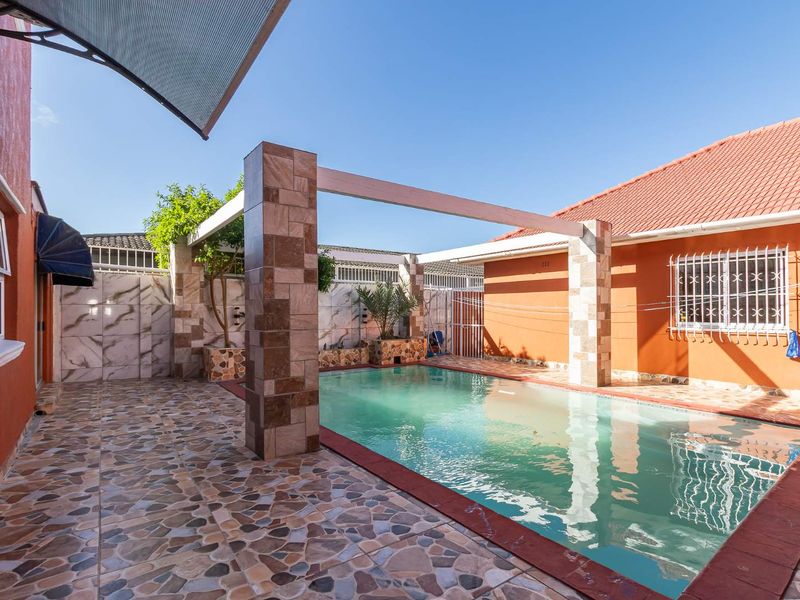 Outdoor pool area featuring a tiled patio, pergola structure, and secure perimeter fencing, ideal for relaxation and entertainment.