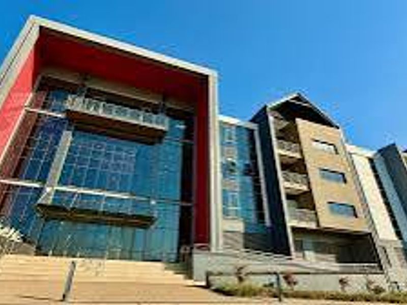 Modern multi-story office building featuring a striking glass facade, red architectural accents, and integrated balconies with steel railings.
